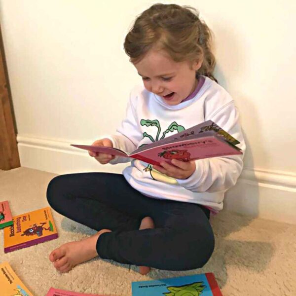 Image of a child sitting on the floor reading a Foodies Books veggie patch story, laughing out loud at the pictures, with other books lying around nearby.